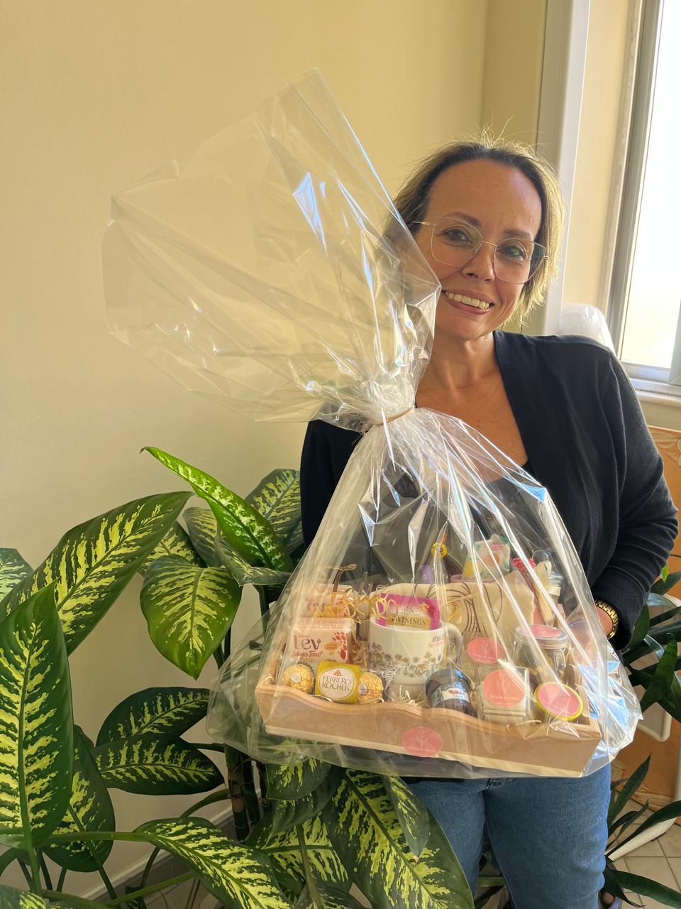 Renata com óculos e sua cesta de aniversário perto das plantas